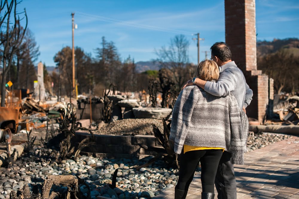 Man and woman with their backs to camera as they examine ruins of house destroyed by fire