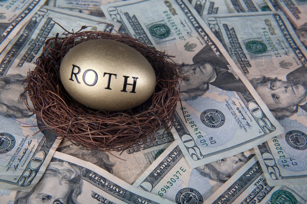 A golden egg with the letters ROTH in a bird's nest on top of money spread out on a table