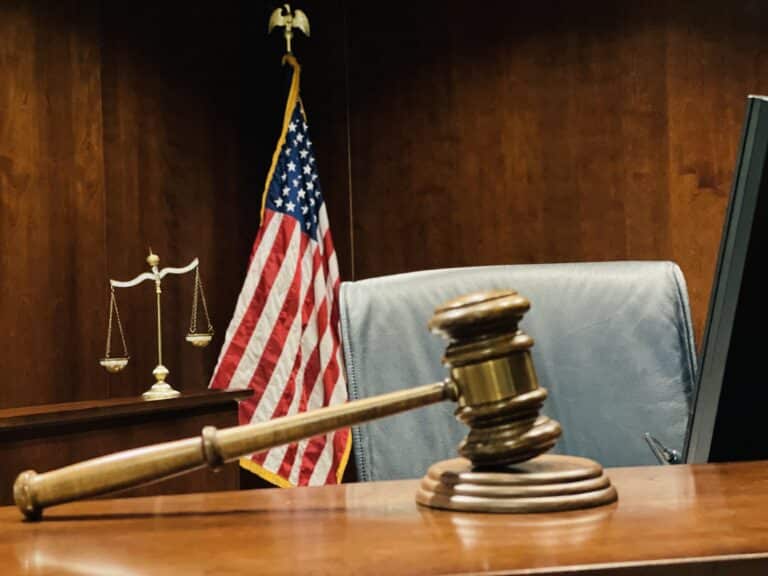 Judge's wooden gavel on judicial bench with scales of justice and American flag in background