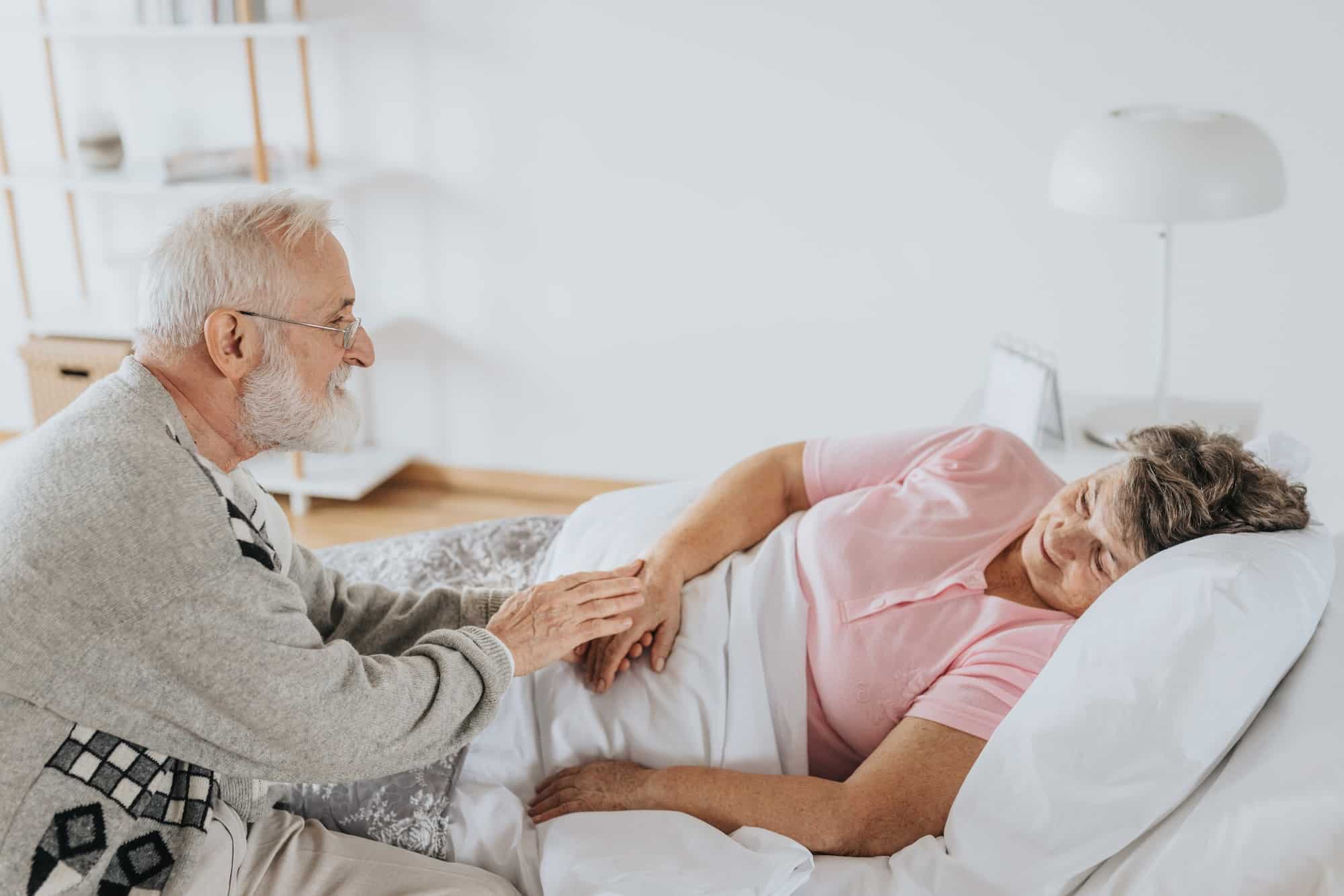 Husband sitting on bed spending time with bedridden wife
